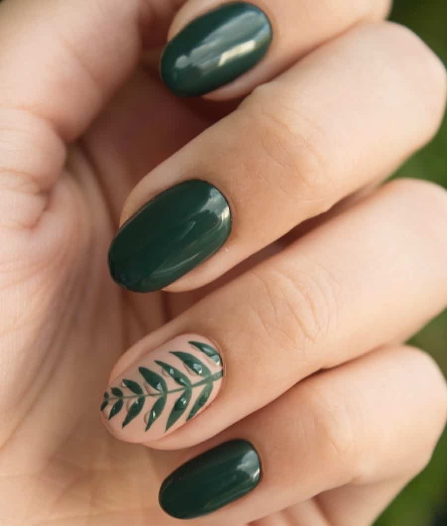 a hand with solid-colored dark green nails and one matte nude accent nail with green leaf art