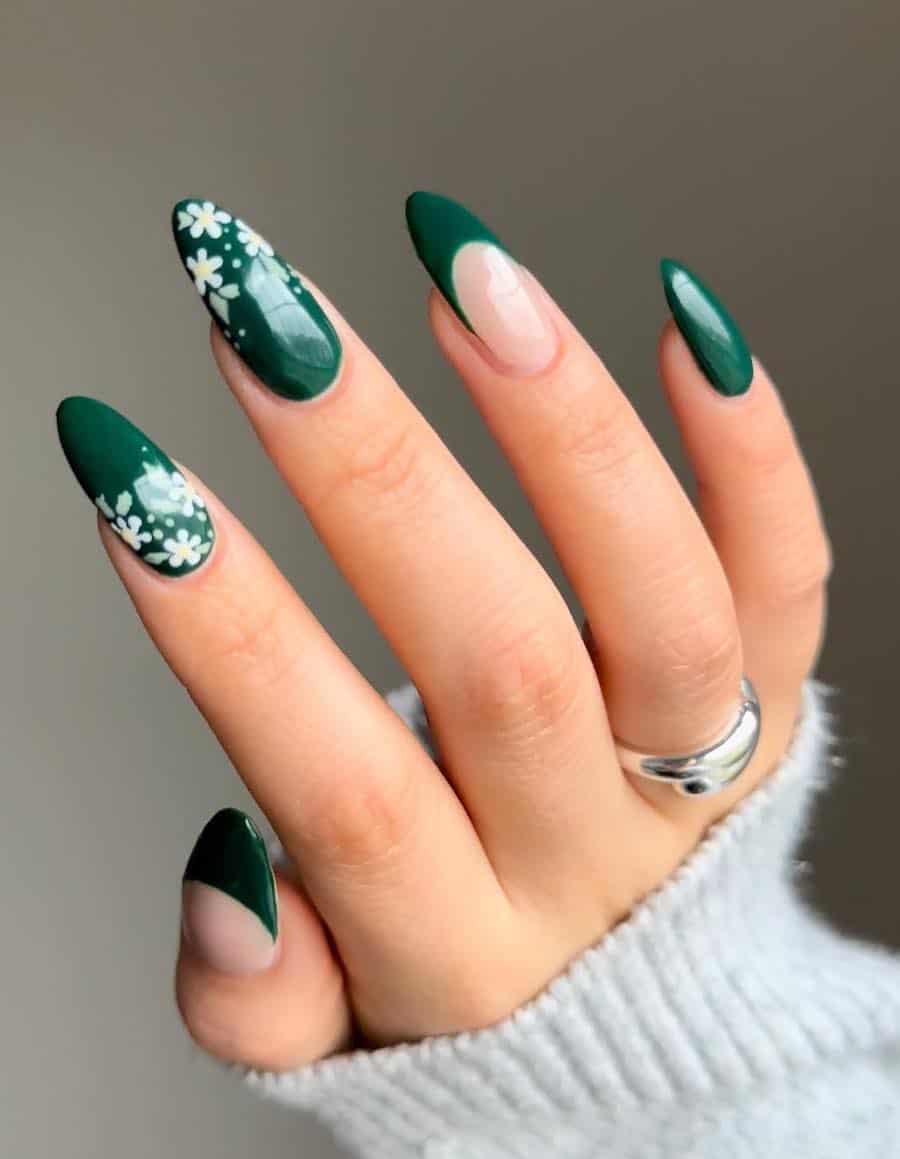 a hand with long almond nails painted in dark green with white floral accents and French tip accent nails