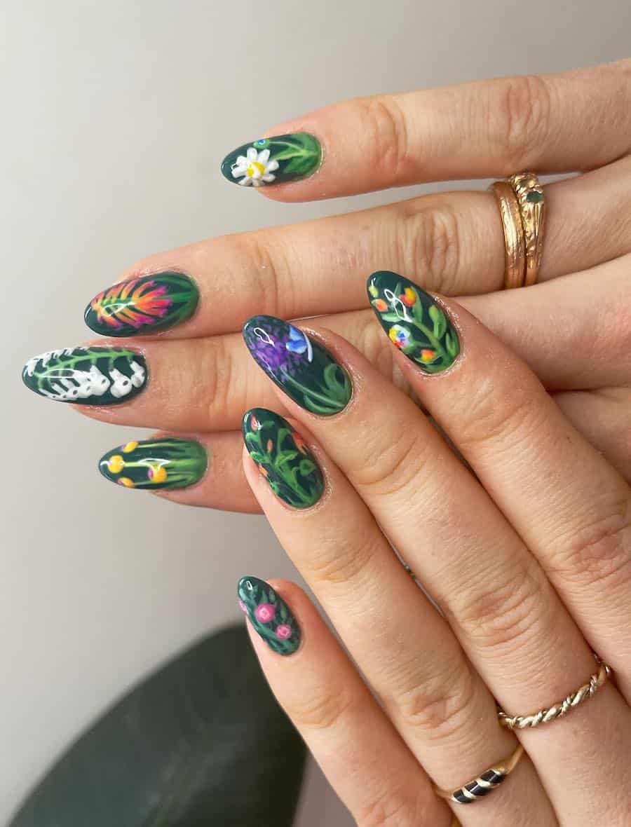 a hand with medium-long almond nails painted a dark green shade with colorful floral nail art