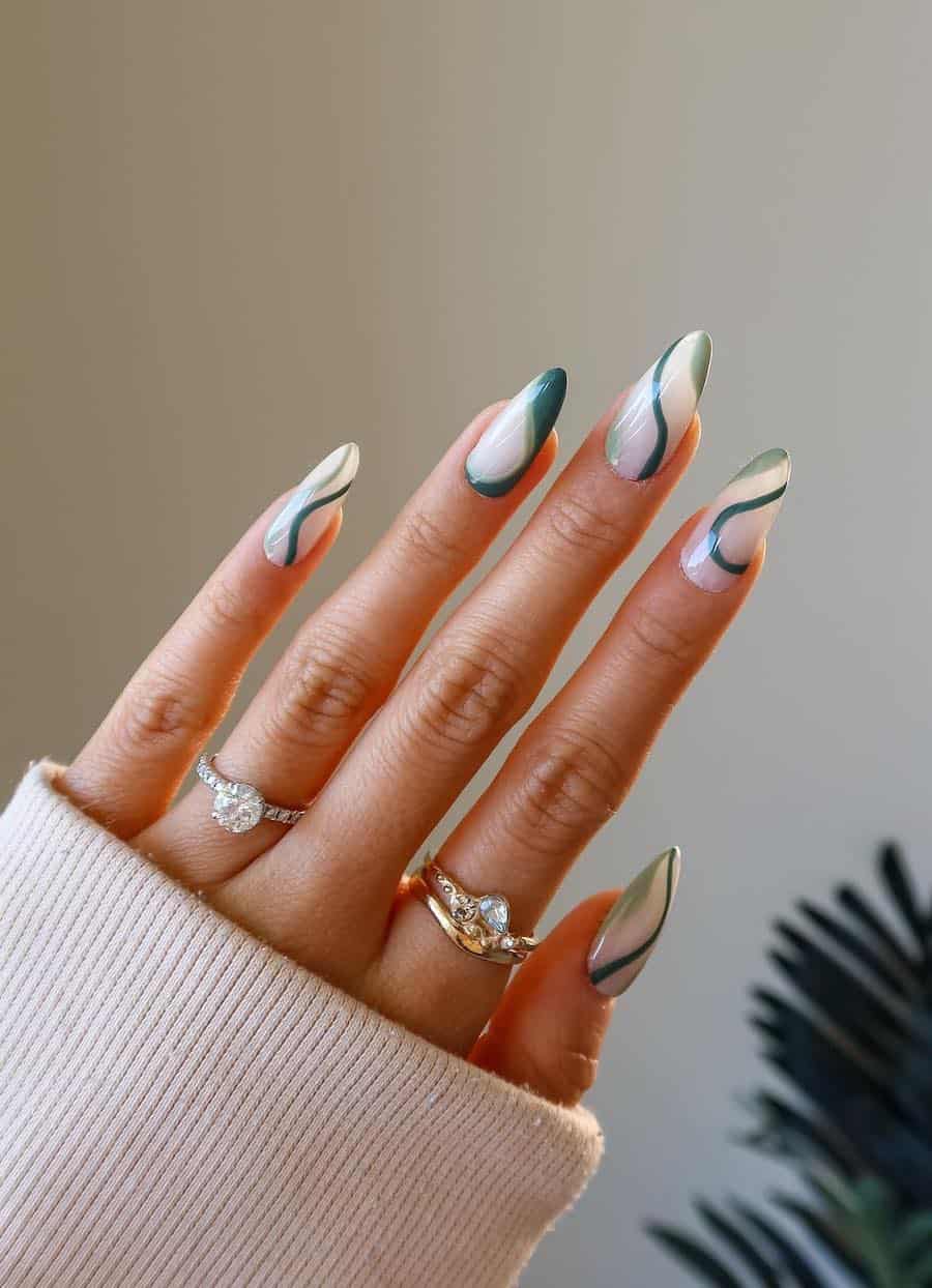 a hand with long milky white almond nails with olive green and forest green swirl accents